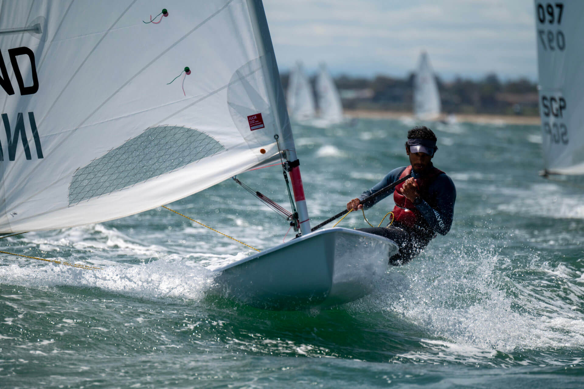 USC Viterbi mechanical engineering student Upamanyu Dutta in a sailboat tugging and leaning toward the right to accelerate over the other sailboats in the race, pictured in the background. 