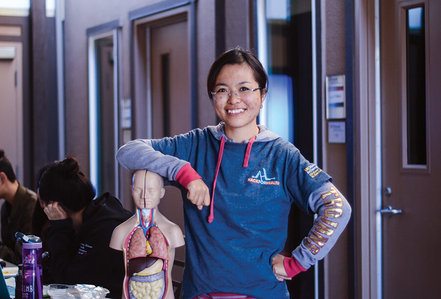 Thủy Truong poses with her arm on top of a miniaturized model of the human body at an event called Hack for Health.